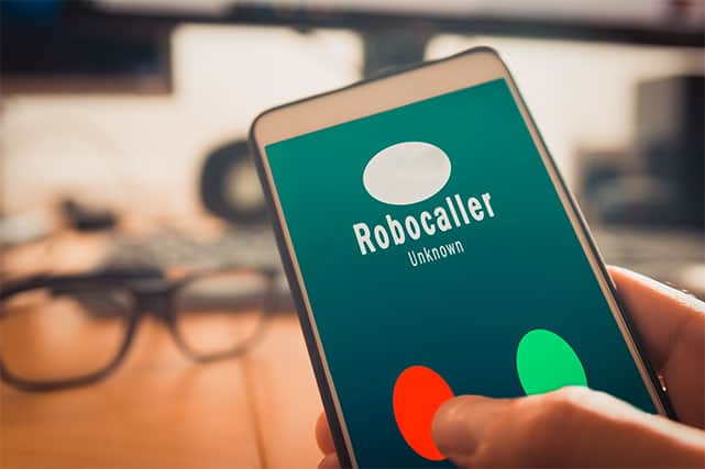 An image featuring a person holding his cellphone and a robocaller is calling him representing a spam call
