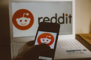 An image featuring a person holding his phone and a laptop in the background that has both Reddit opened